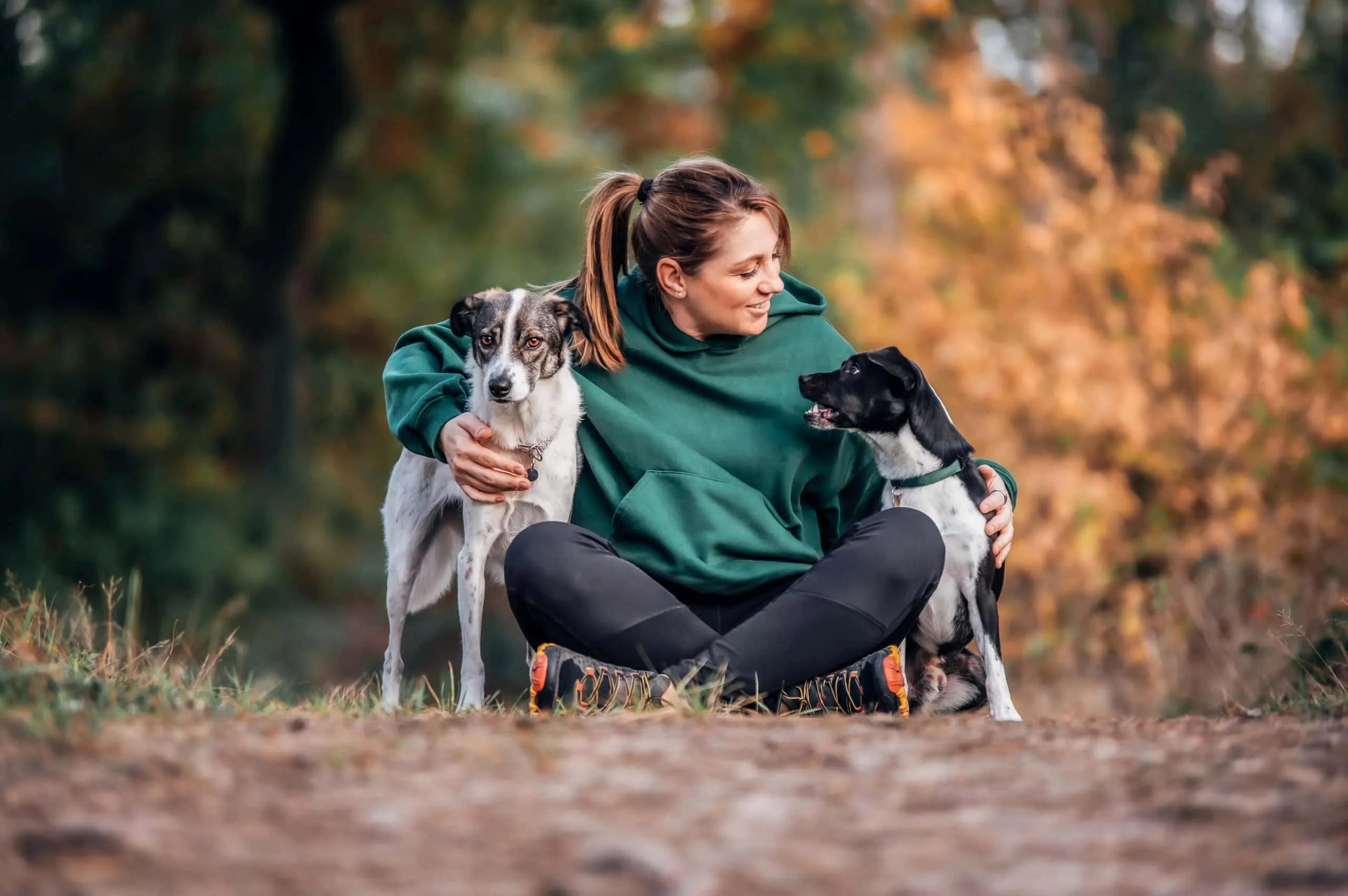 Steffi sitzt mit ihren beiden Hunden im herbstlichen Wald