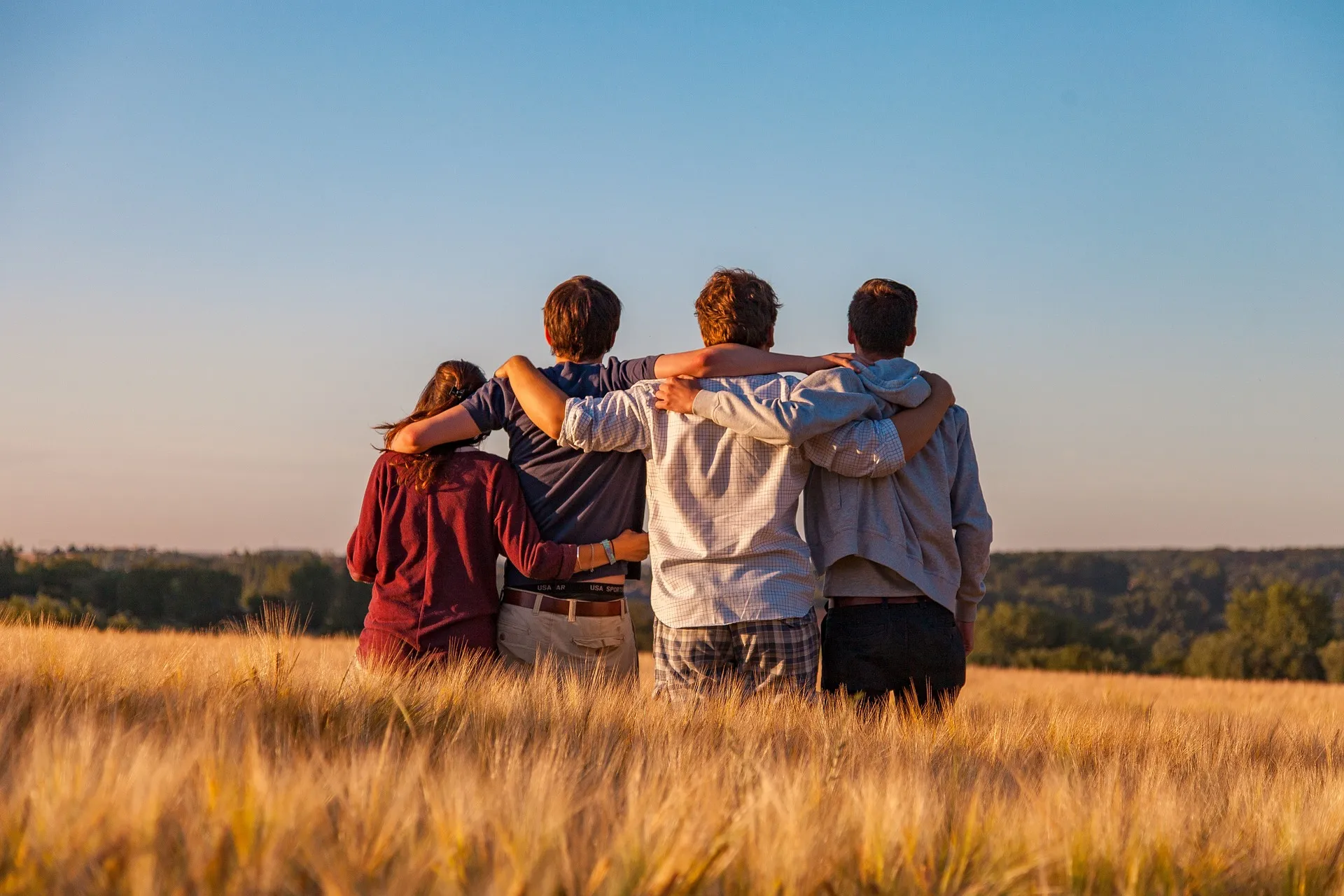 Vier Freund*innen stehen Arm in Arm in einem Getreidefeld und blicken in die Ferne