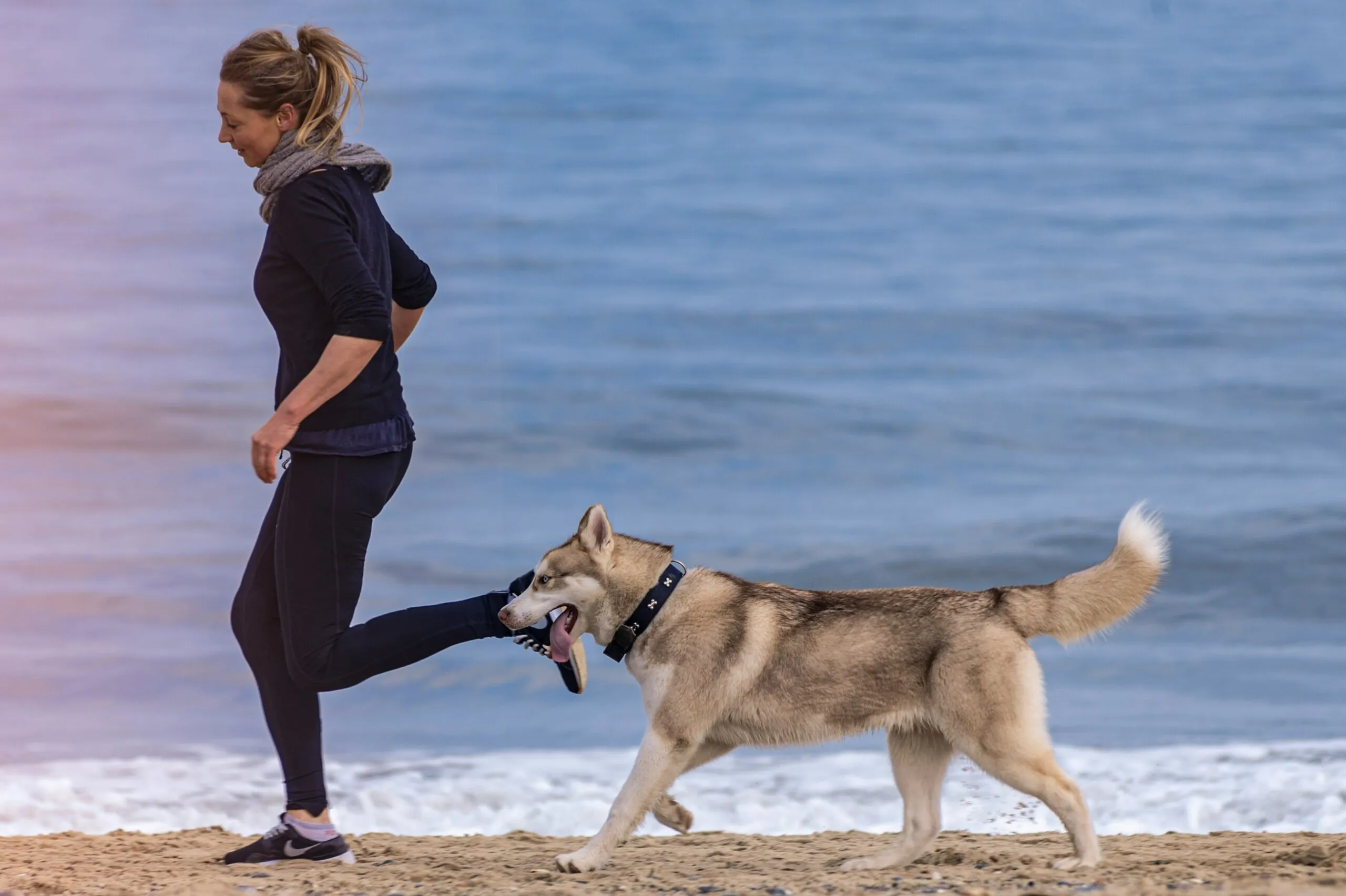 Frau joggt am Strand mit ihrem Hund an der Leine
